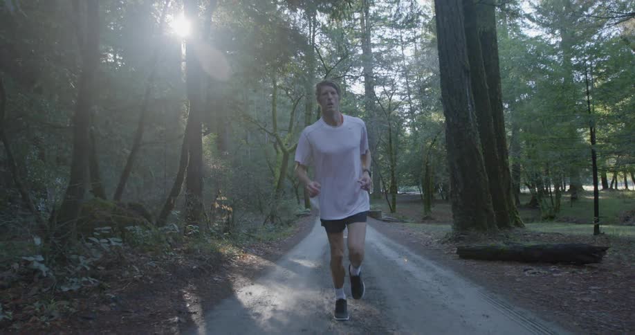 A man is jogging on a narrow path in the park