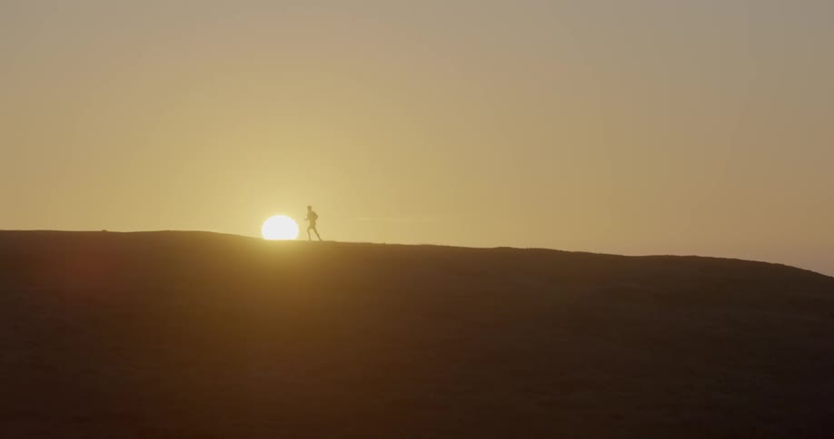 A man runs over a hill as the sun is about to set