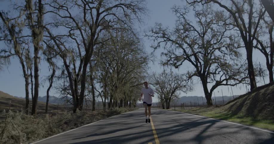 A man jogs down a tree lined street in the daytime