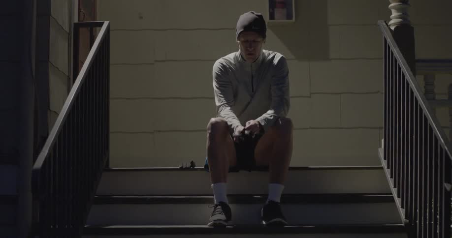Man sitting on the stairs ties his shoelaces and wears his gloves before he starts jogging