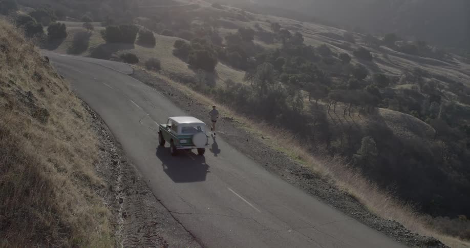 A person runs down a hillside road as a car passes