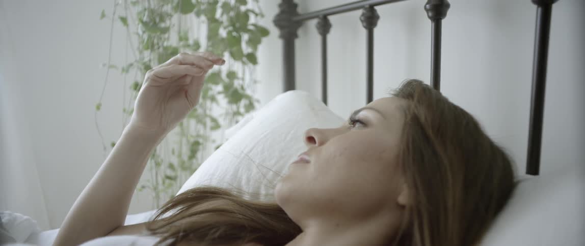 A woman lays in bed messing with her hair