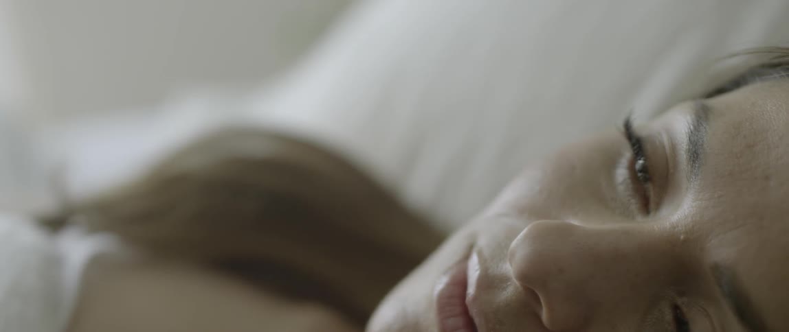A woman sleeping in a bed opens her eyes