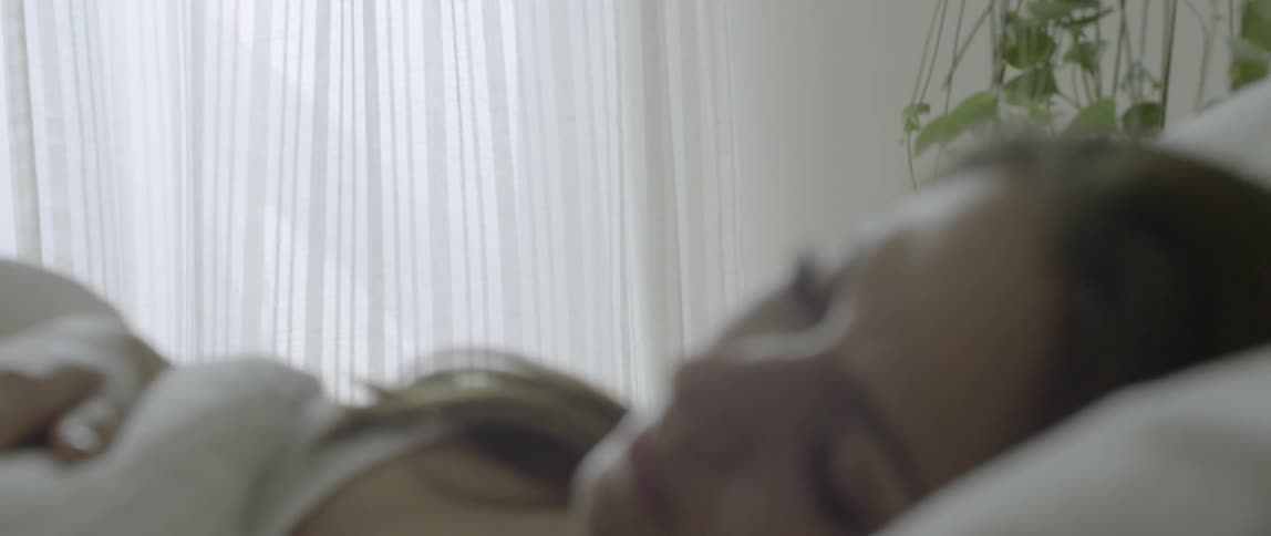Curtains blow in a window where a woman is resting in bed