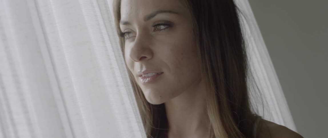 A woman standing between a set of curtains looks back into a room then turns away