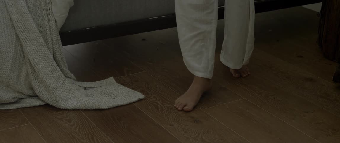 A woman walks on the floor next to a bed