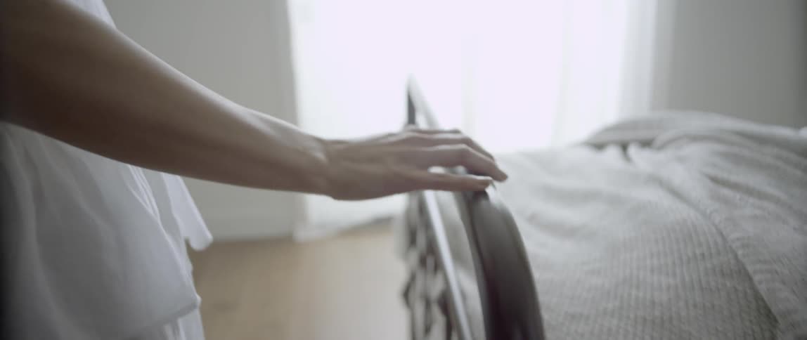A woman walks around to the front of a bed