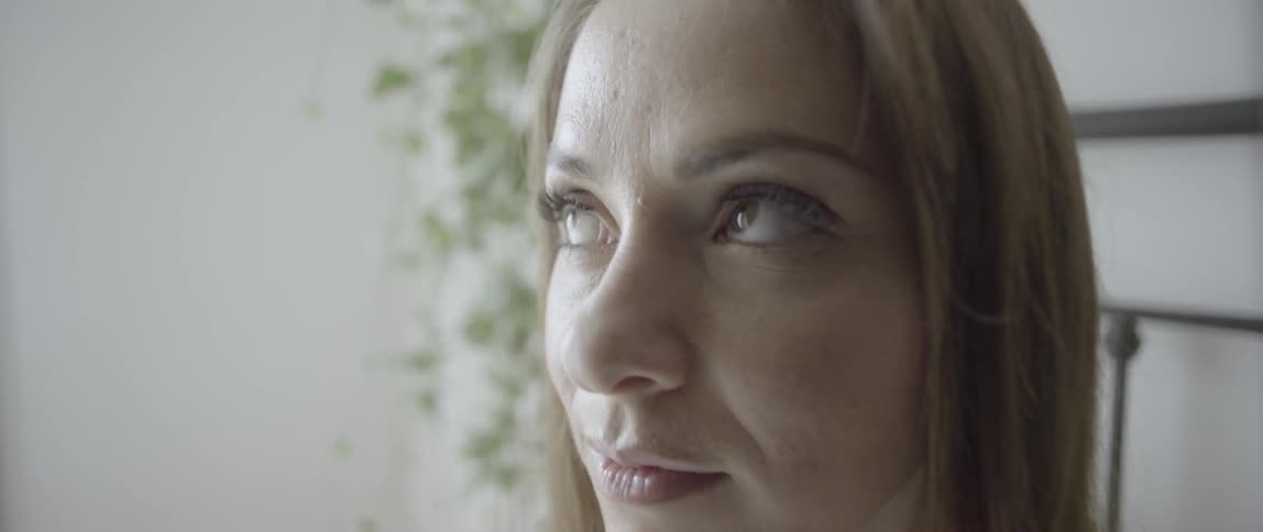 A woman sits in bed and brushes her hair from her face
