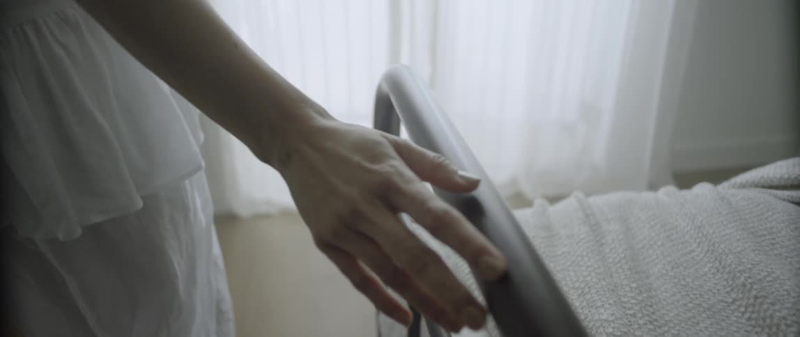 A woman touches the brass rail on a bed as she walks towards a window
