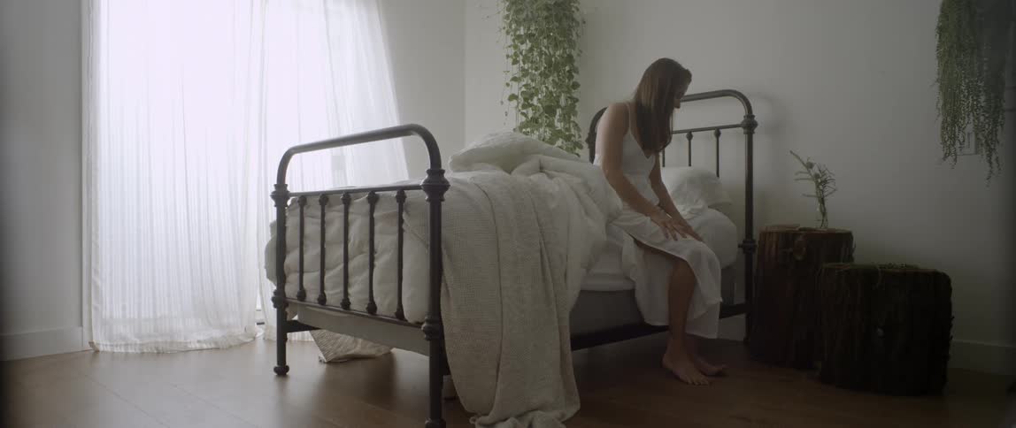 A woman sits on the edge of a bed