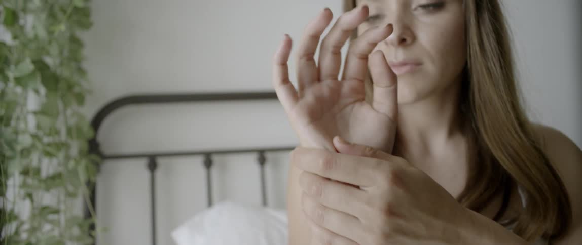 A woman lays in bed rubbing her arm