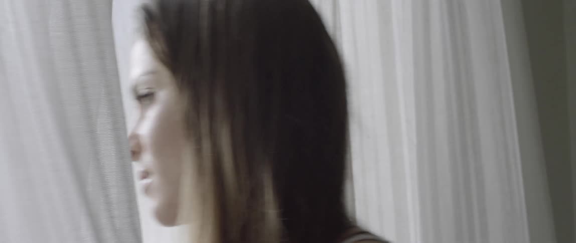 A woman looks outside then steps through a pair of curtains