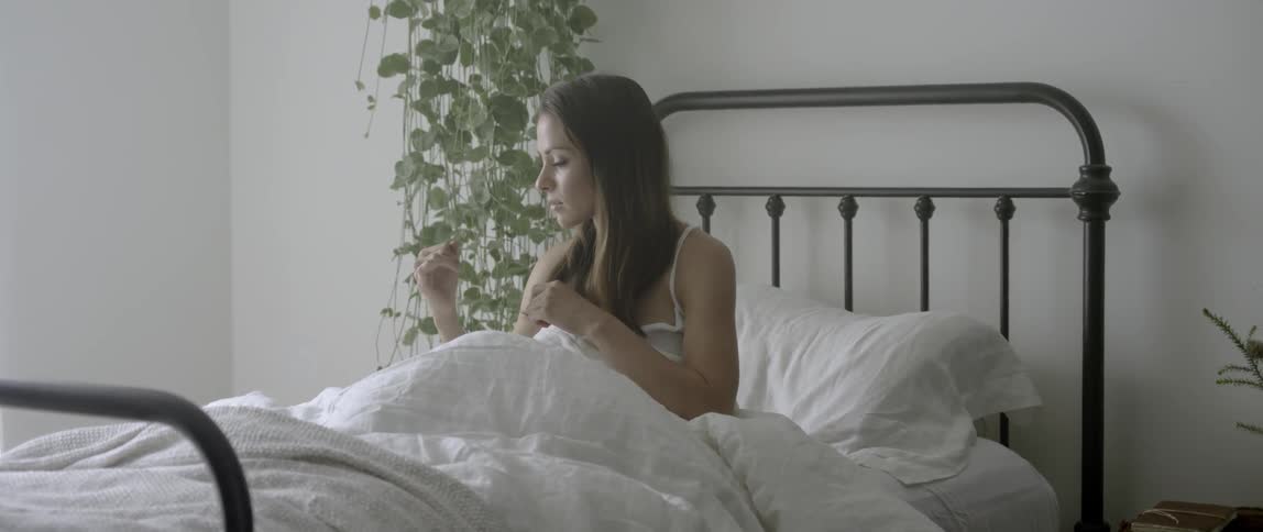 A woman sits in bed fiddling with her hair