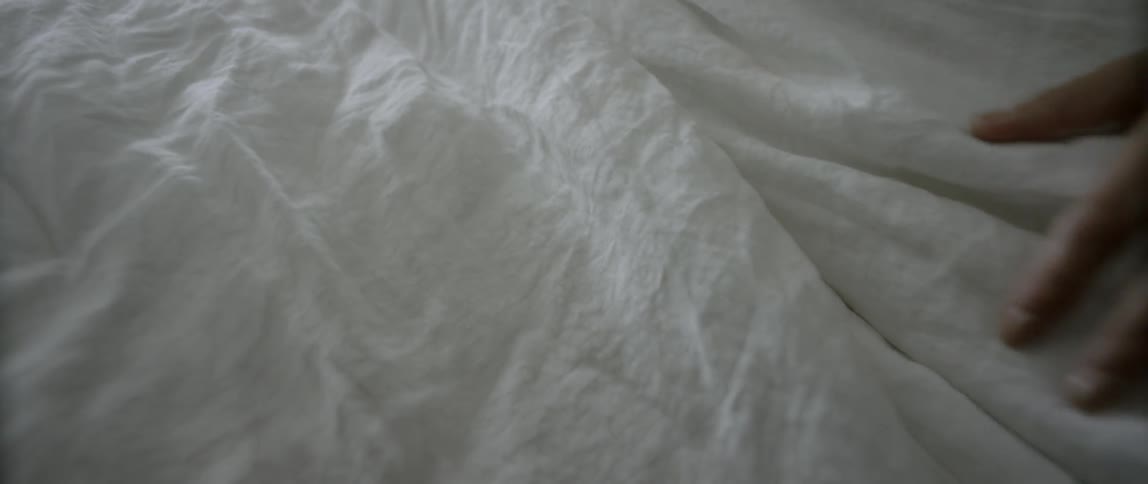 A woman sitting in bed feels the covers before pulling them back