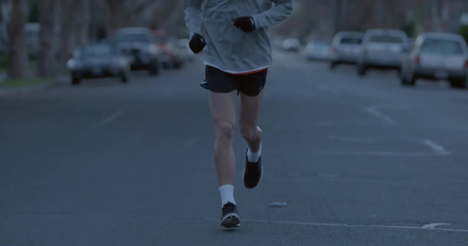 Man running down a street with cars parked behind him
