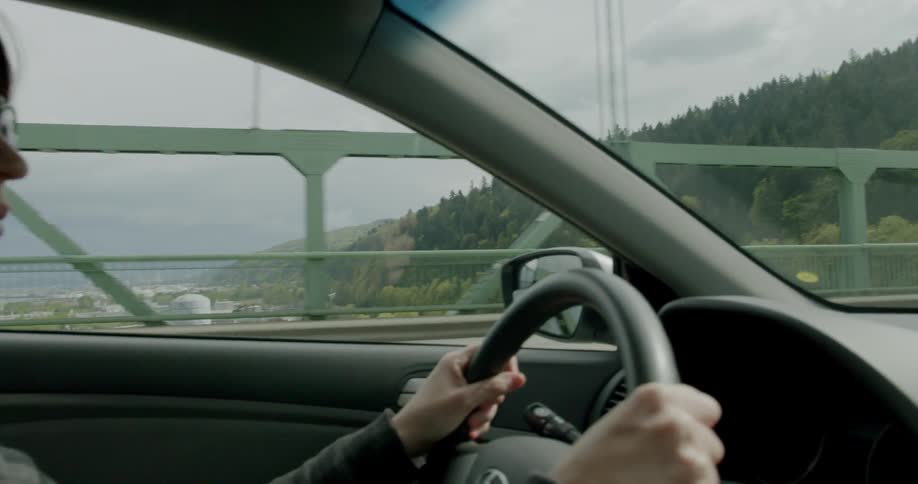A woman driving a car across a bridge