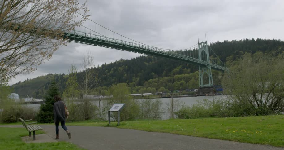 Woman walking through park with bridge in background