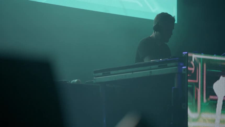 A dj performs on a stage under flashing lights