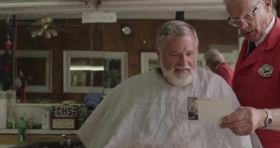 Barber showing a photograph to an old man sitting in his salon