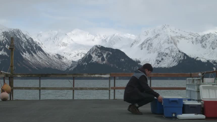 A white man walks across the deck of a ship to check on a plastic bin