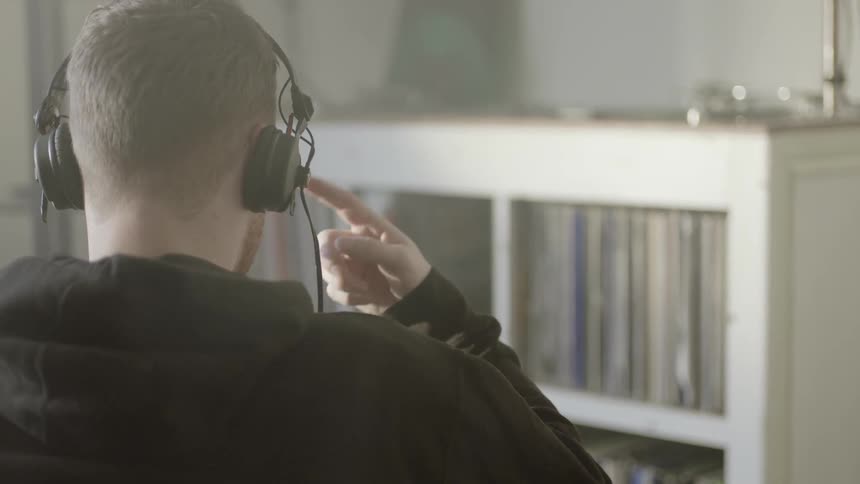 A man is sitting down listening to music on headphones