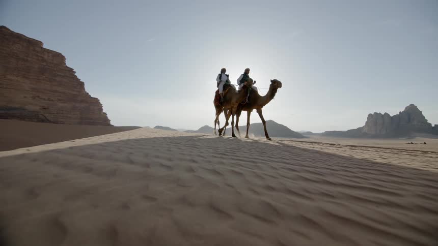 Two people ride camels side by side in the desert