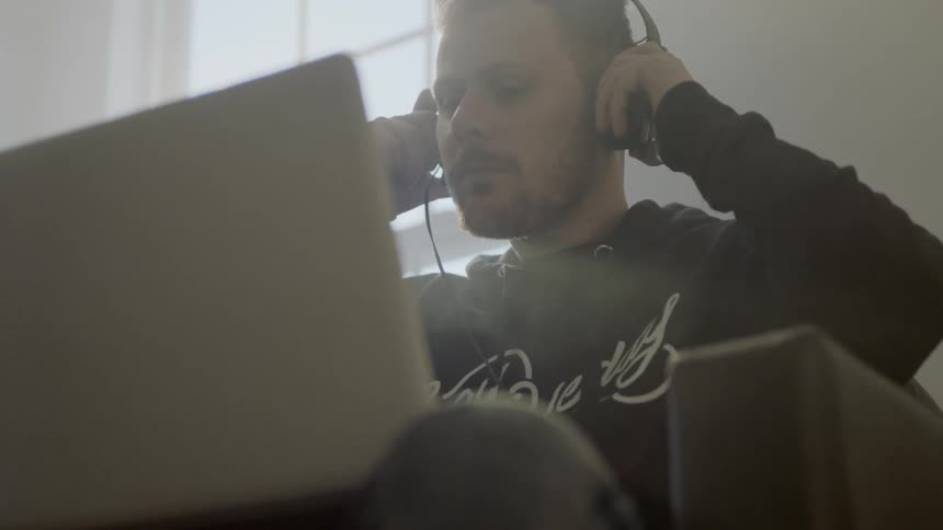A man working on a laptop takes off his earphones and thinks about something