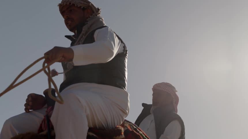 A man bounces in the saddle as he rides a camel