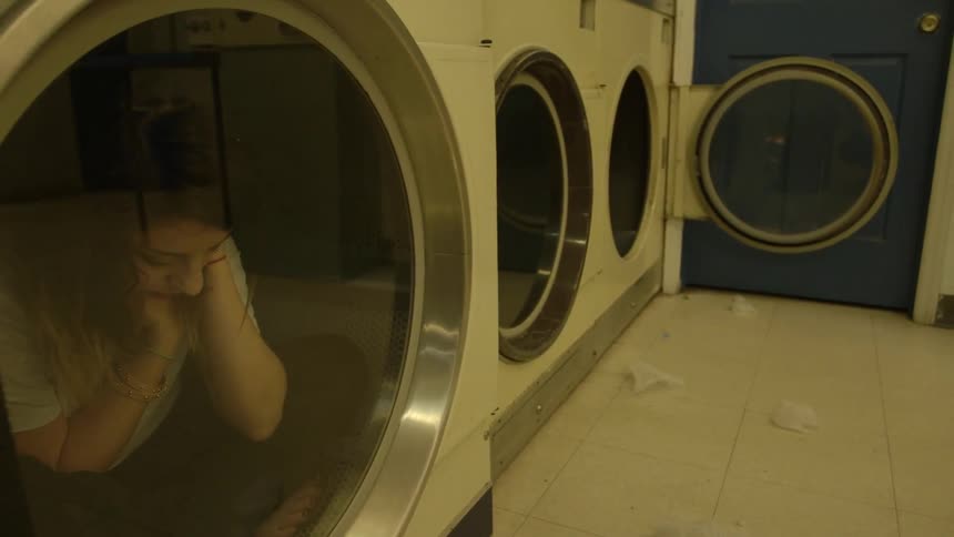 A woman sits inside a laundromat dryer