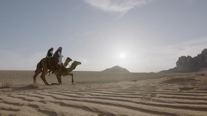 Two people ride camels in the desert