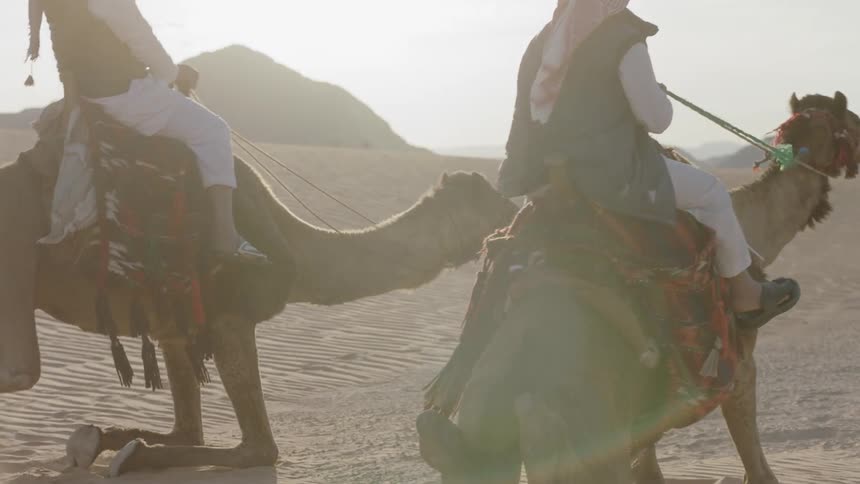 Two people ride camels in the desert
