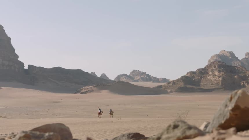 Two people are riding camels across the desert