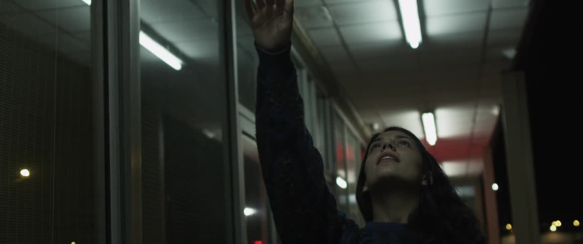 A woman stand in a hallway and leans back with her arm up