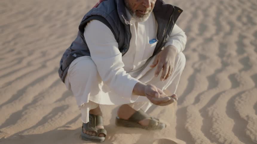 A man kneels and sifts through desert sand