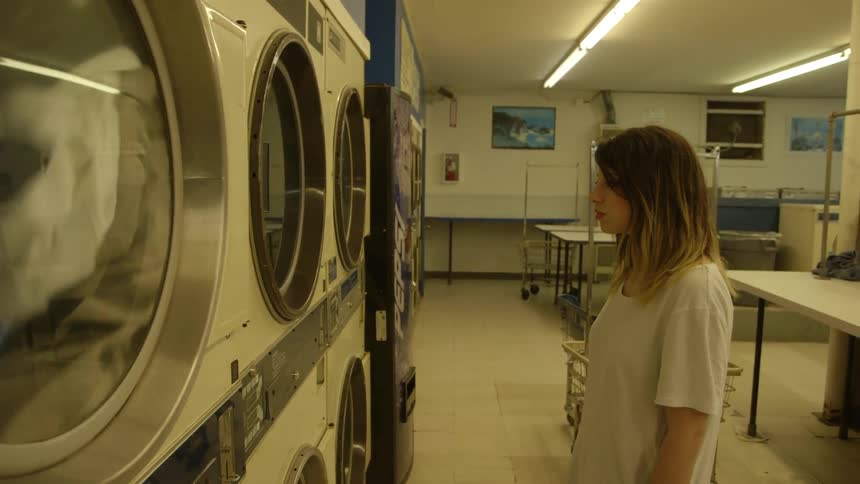A woman is watching the clothes spin in a dryer at the laundromat