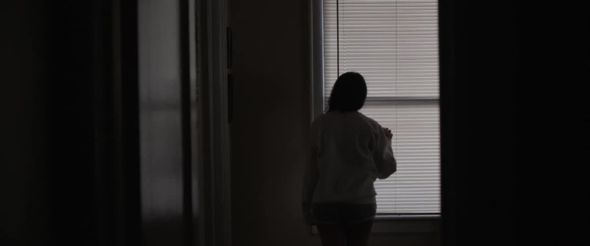 A woman is peeking through the shades on her window