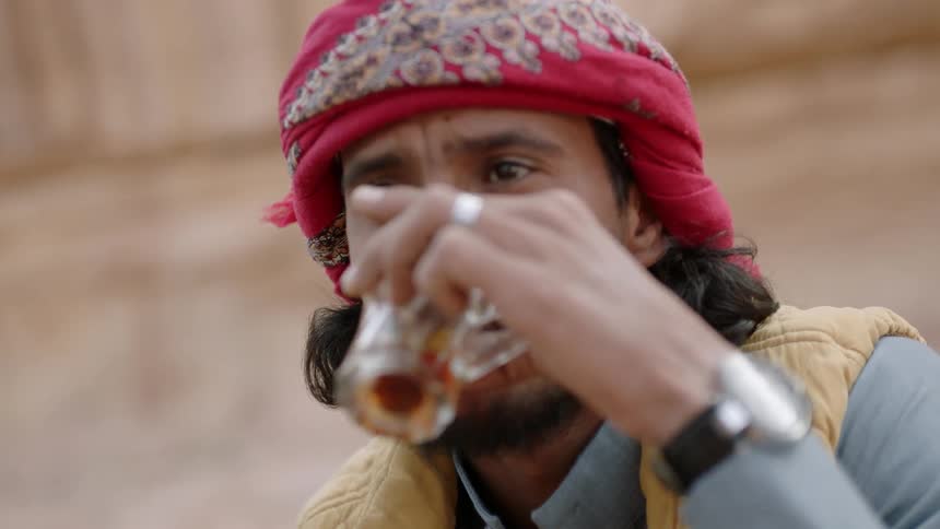 A man in traditional headgear drinks tea outside