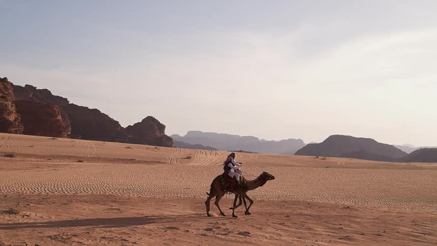 Two people ride camels side by side in the desert