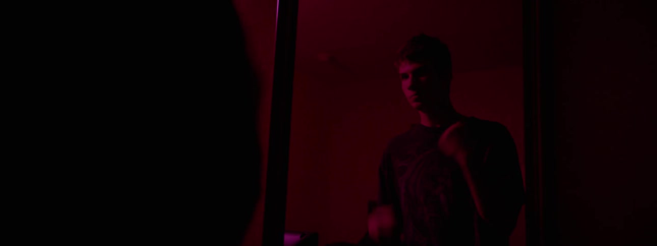 A man is standing in a dark room punching himself in the face