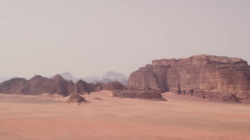Mountains sit in the desert surrounded by sand