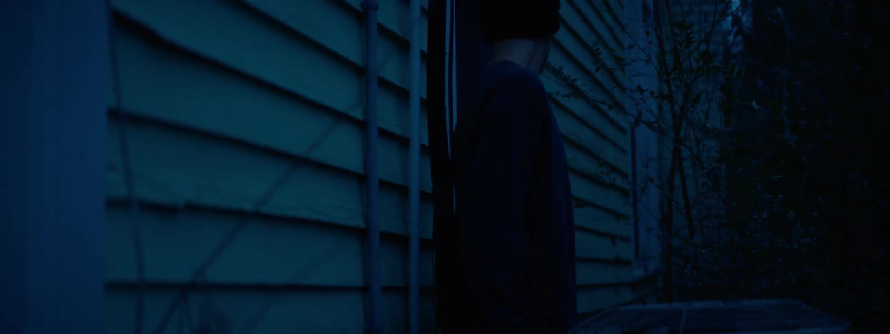 A man is walking beside a house looking in the windows