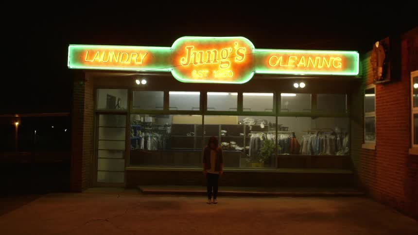 A woman stands outside of a dry cleaner's at night