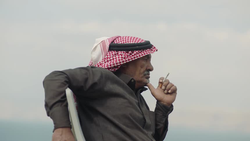 An Arab in traditional headgear smokes a cigarette outside
