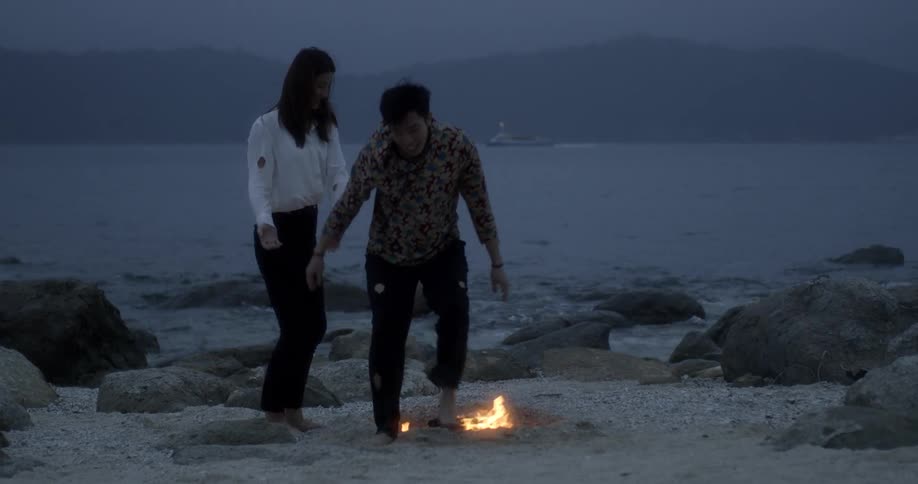 A man and woman are dancing around a fire on the beach