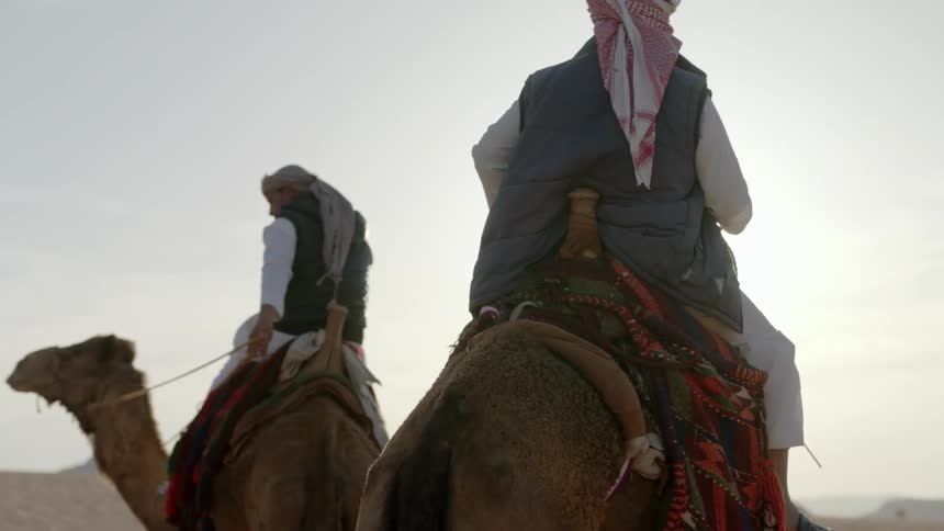 Two men are riding camels in the desert