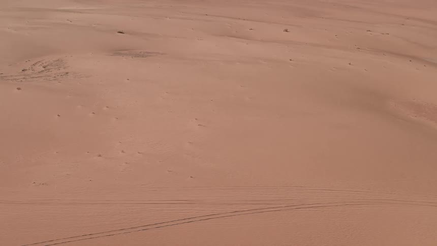 Tire tracks mark the sand in front of a large rock formation