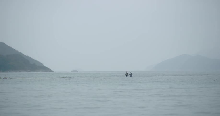 Two people walk in knee deep ocean water