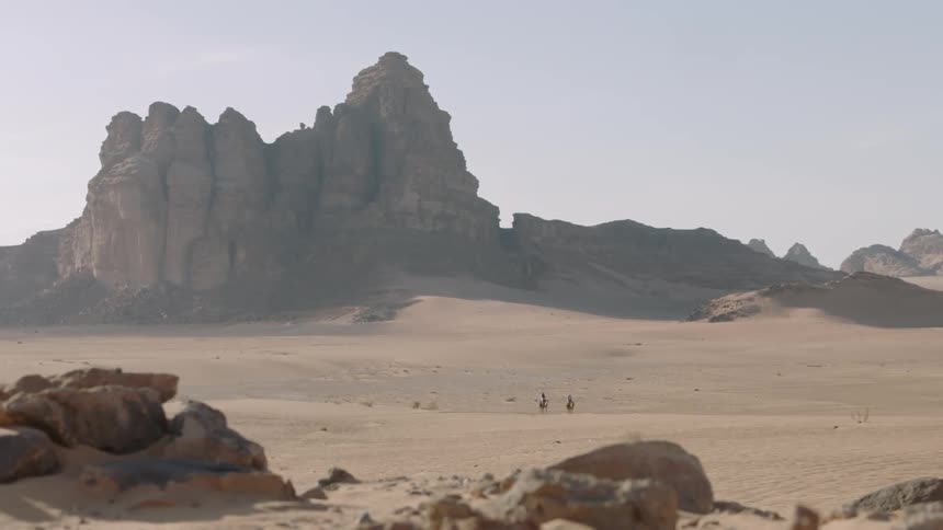 Two people ride camels in the desert