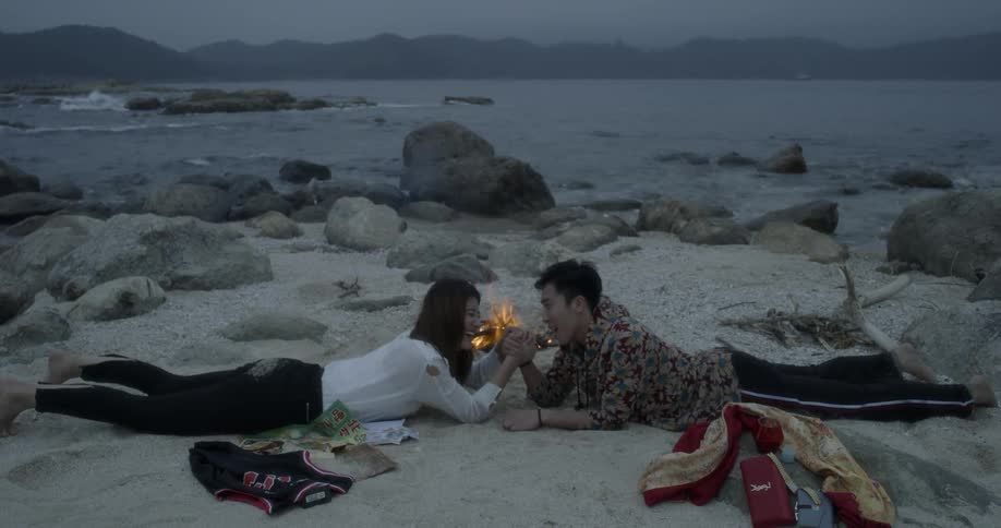 A couple lying on beach are arm wrestling