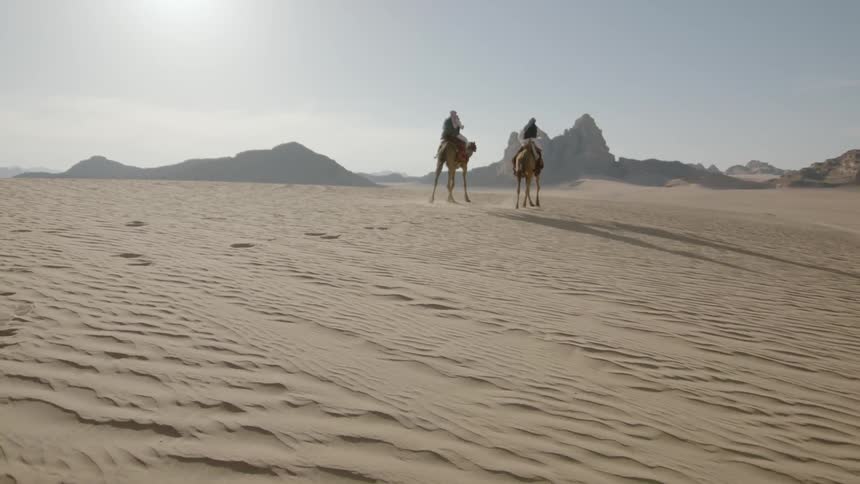 Two people ride their camels through the desert